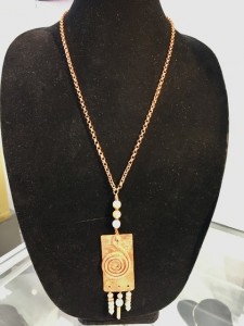 Long rectangular copper piece with coiled copper and white round clay beads.
